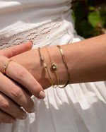 Gold bracelet stack featuring a gold chain charm bracelet, a gold stacking bracelet and a cuff bangle bracelet on model. 