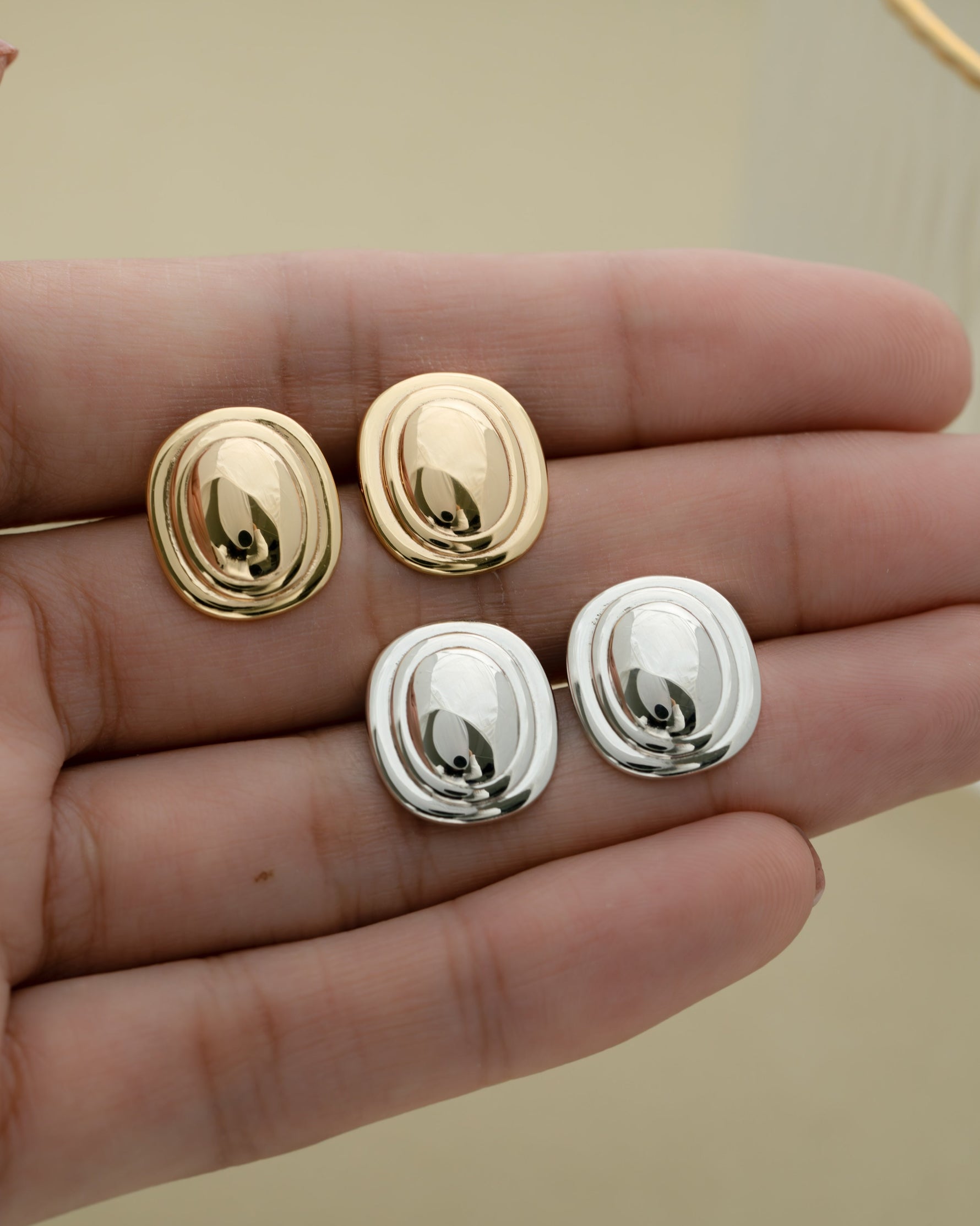 Gold plated earrings and sterling silver minimalist earrings on the palm of a hand