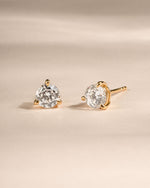 Pair of gold diamond stud earrings on a beige background