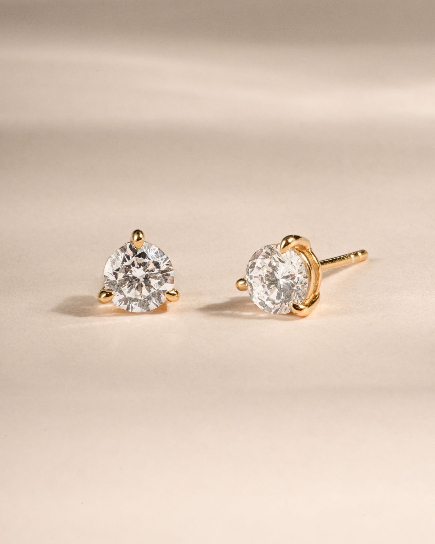 Pair of gold diamond stud earrings on a beige background