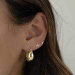 model wearing chunky gold hoops, paired with dainty diamond stud earrings, paired with a tiny stud earring