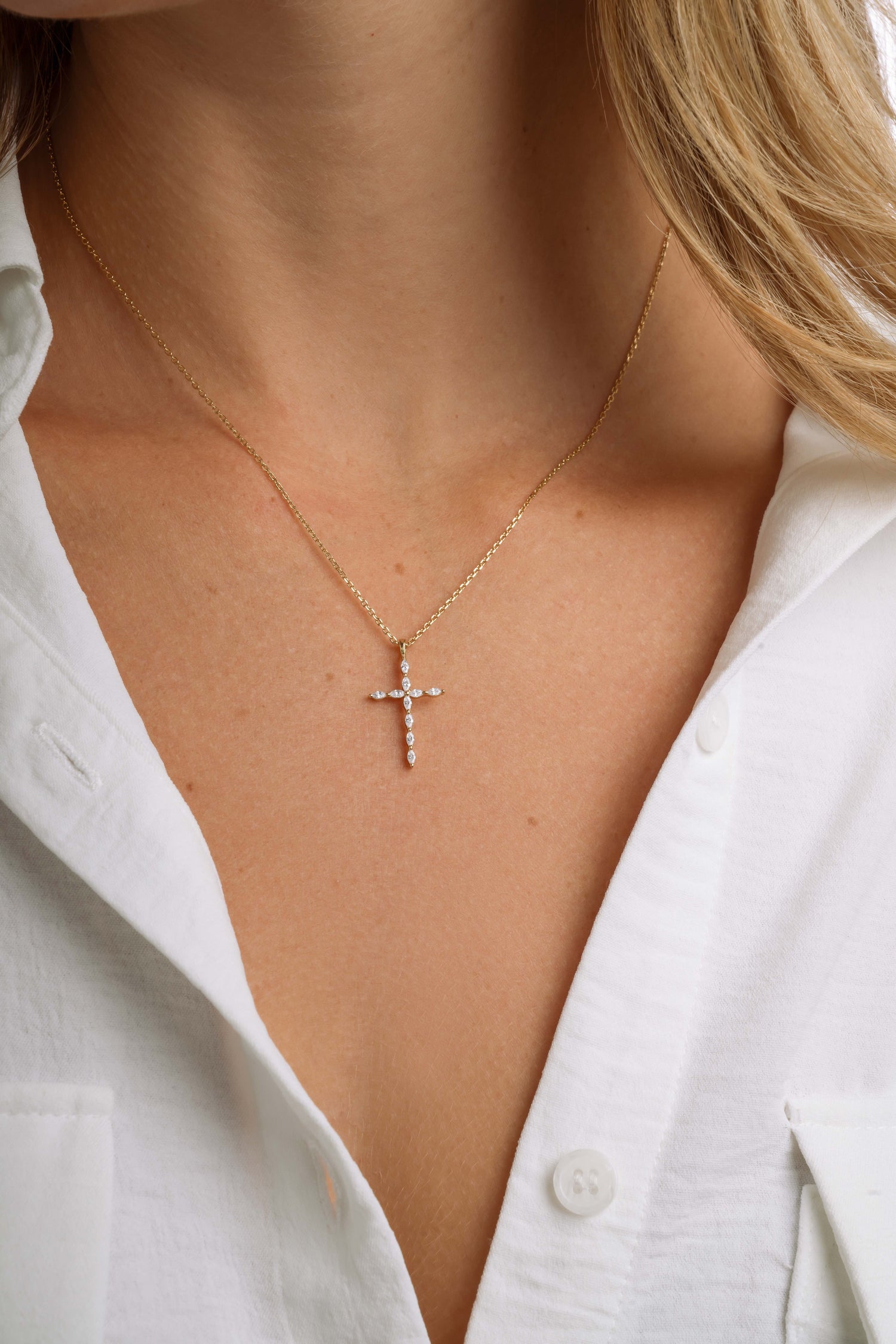 Close-up of a model wearing a gold cross necklace with a white shirt.