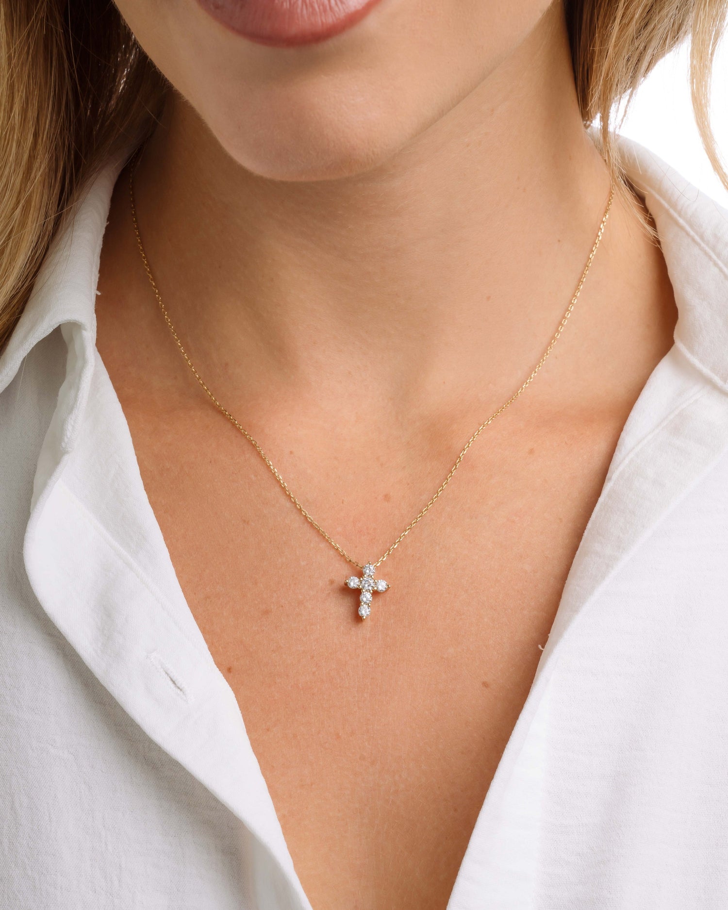 Close-up of a necklace with a cross pendant worn by a person in a white shirt.