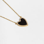Close-up of a gold necklace with a black heart pendant with a black stone and pave diamond details