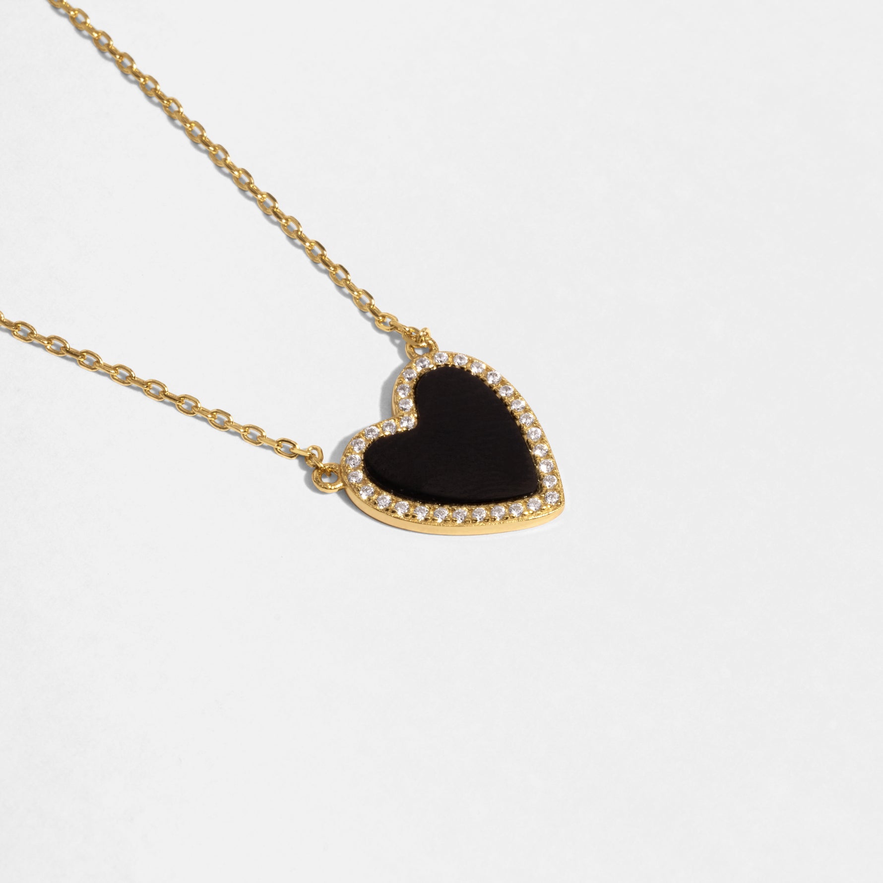 Close-up of a gold necklace with a black heart pendant with a black stone and pave diamond details