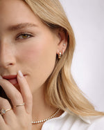 Model wearing celestial hoops, followed by diamond huggie earrings, and a pear cut stud earring. Model is also wearing diamond rings and a round bezel tennis necklace
