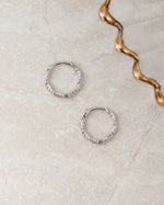 Two sterling silver huggie hoop earrings on a textured beige surfae