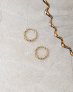 Gold hoop earrings, also can be a cartilage hoop,  on a textured beige surface