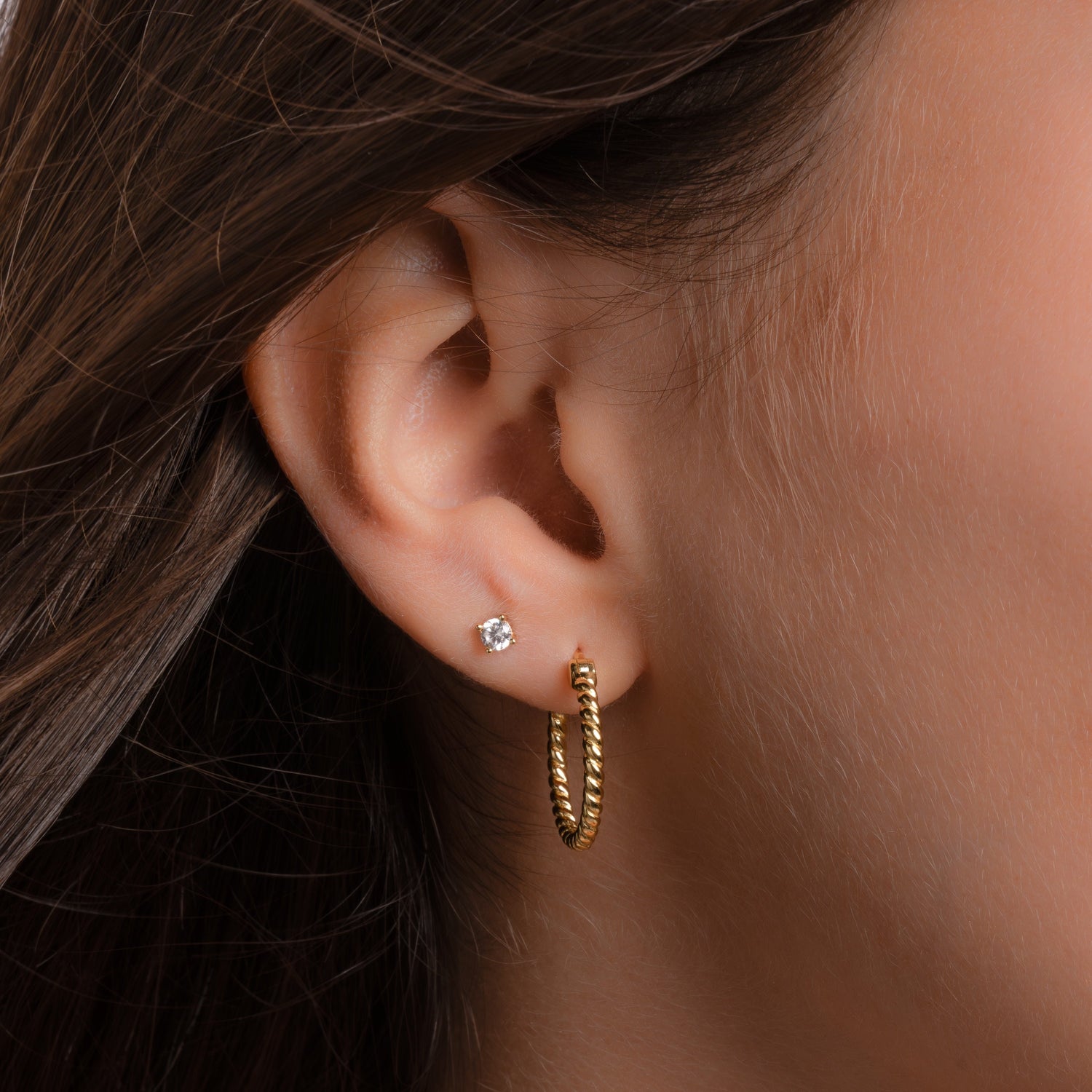 Model wearing dainty gold hoops with spiral design, and a solitaire stud earring