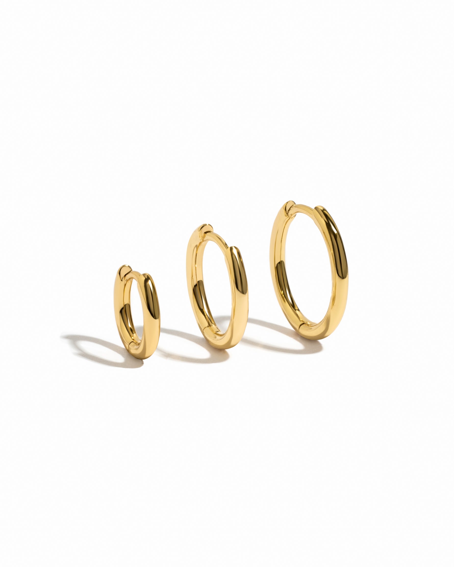Three gold hoop earrings of different sizes on a white background