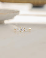 Gold stackable ring with oval cubic zirconia center stone and round cubic zirconia stones surrounding on glass surface