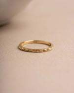 Thin gold stackable ring with a textured band on a beige background