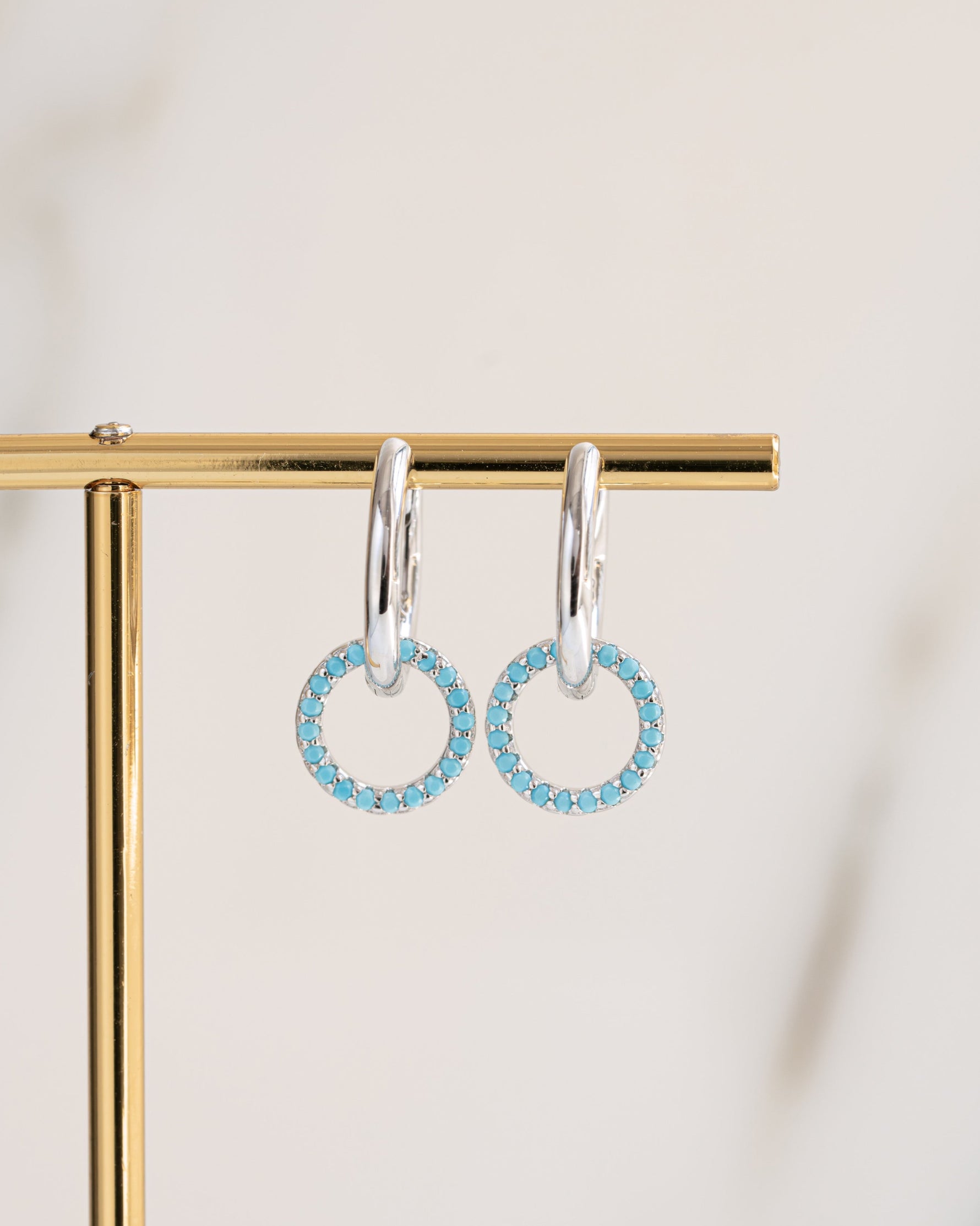 sterling silver blue earrings with a huggie hoop earring design on a gold stand and light background