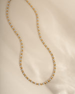 Gold and silver tennis necklace on a beige background
