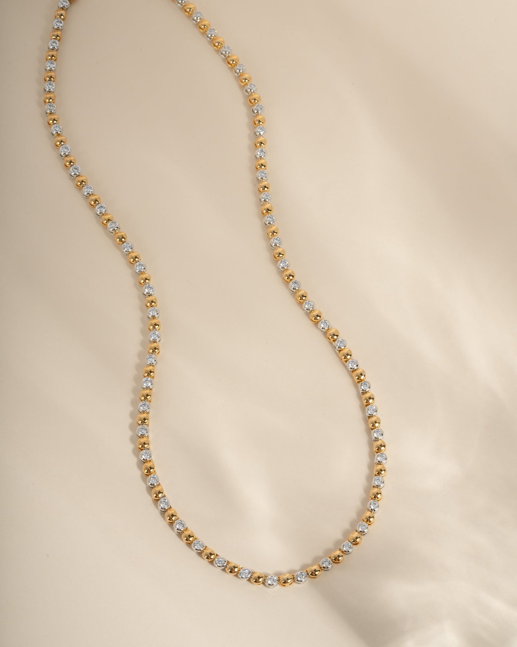 Gold and silver tennis necklace on a beige background