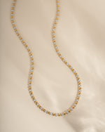 Gold and silver beaded diamond statement necklace on a beige background