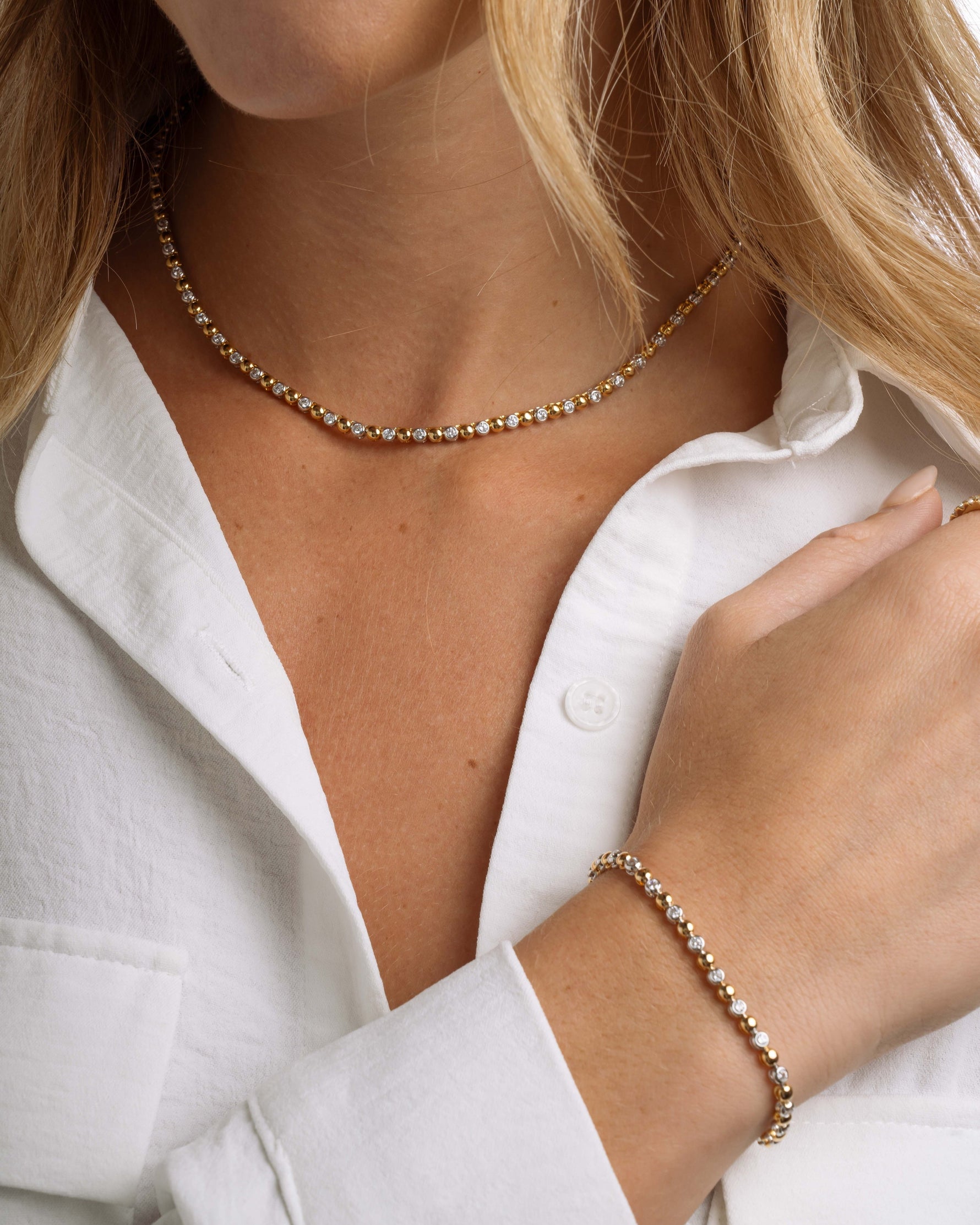 Close-up of a person wearing a mixed metal statement necklace and matching tennis bracelet with a white shirt.