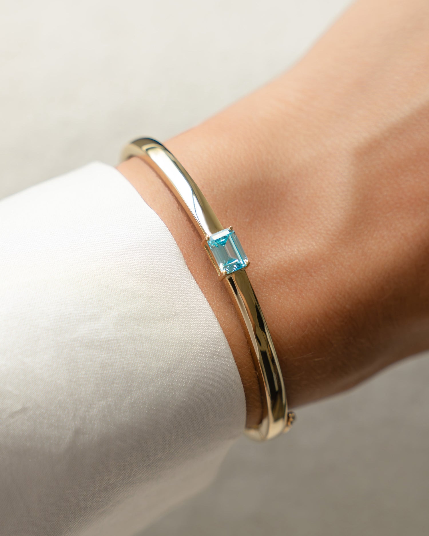 Model wearing gold aquamarine bracelet with a bangle bracelet design