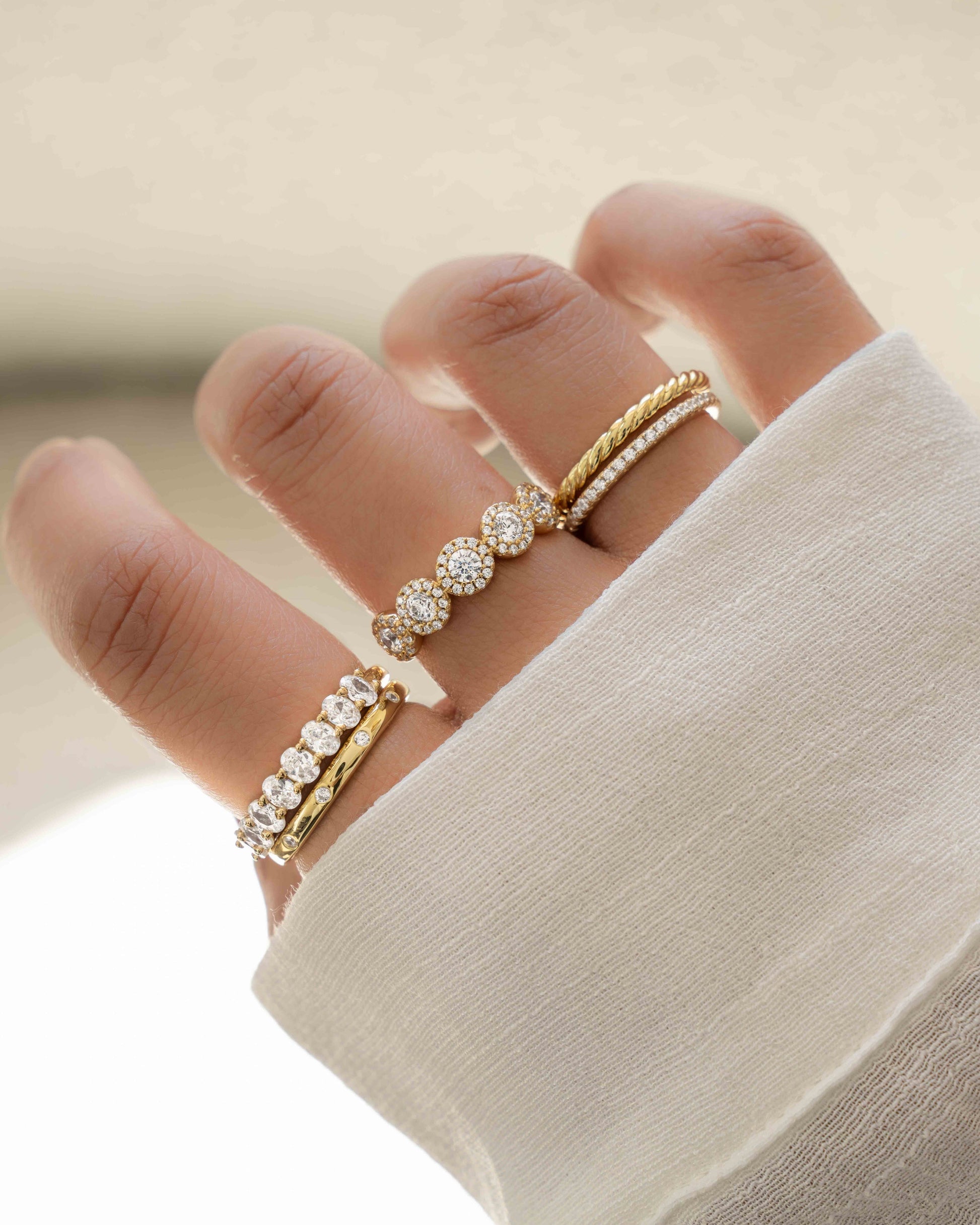 model wearing gold ring stack featuring diamond multi stone ring, oval diamond eternity band, 5 stone halo ring, spiral band ring, cz eternity ring