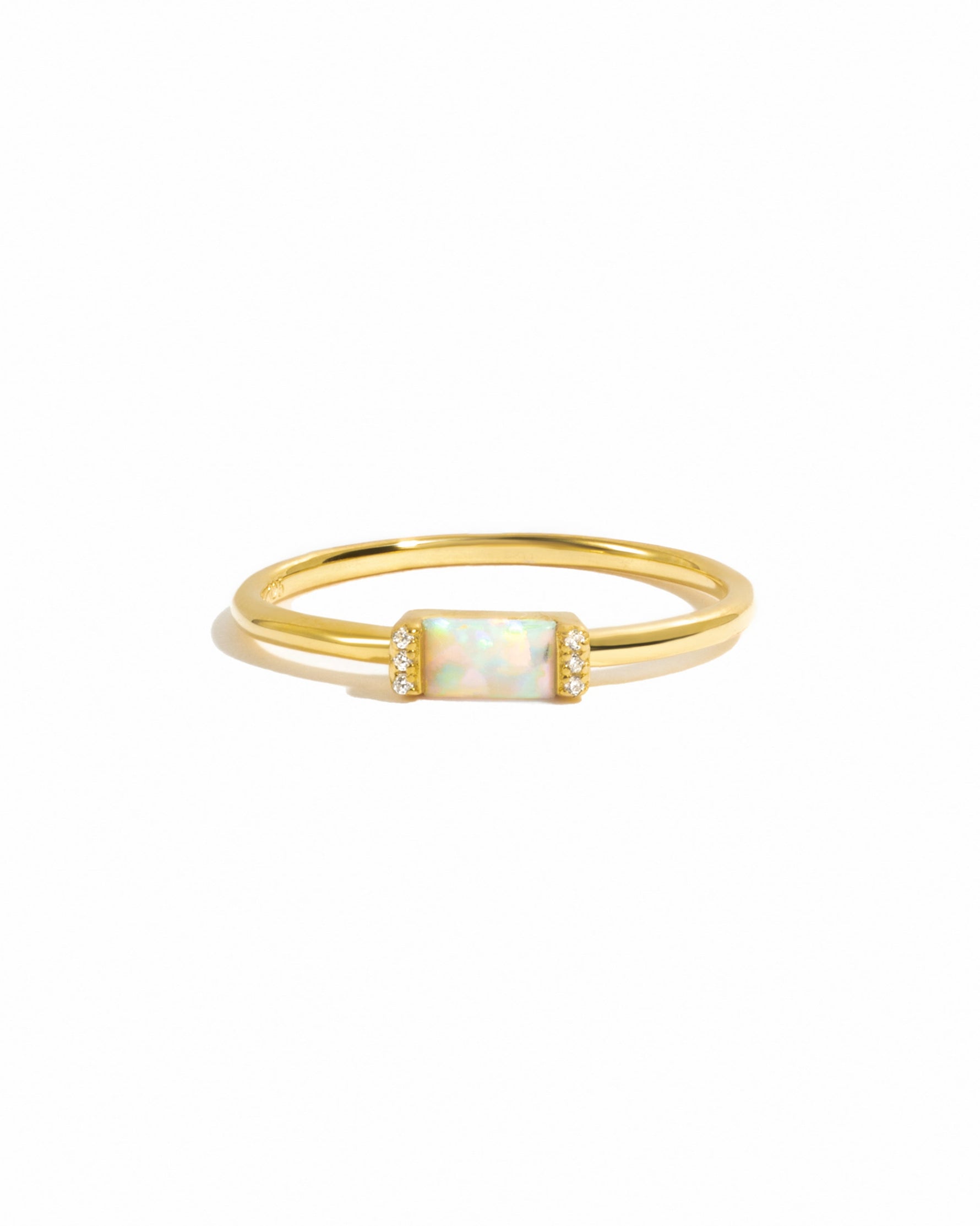 Gold ring with a central opal gemstone and pave cz stones on each side on a white background