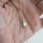 Model's hand showcasing an opal pendant necklace with dainty pave diamonds in plated in 14k gold 