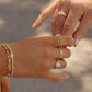 model holding hands with another model, both wearing gold ring stacks featuring an opal oval solitaire statement ring