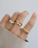 Model wearing three gold dainty rings featuring a gold oval ring, a gold statement ring, a bezel diamond ring, and a gold stackable ring.