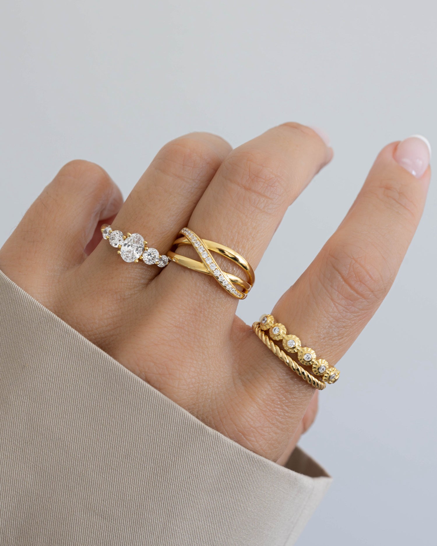 Model wearing three gold dainty rings featuring a gold oval ring, a gold statement ring, a bezel diamond ring, and a gold stackable ring.