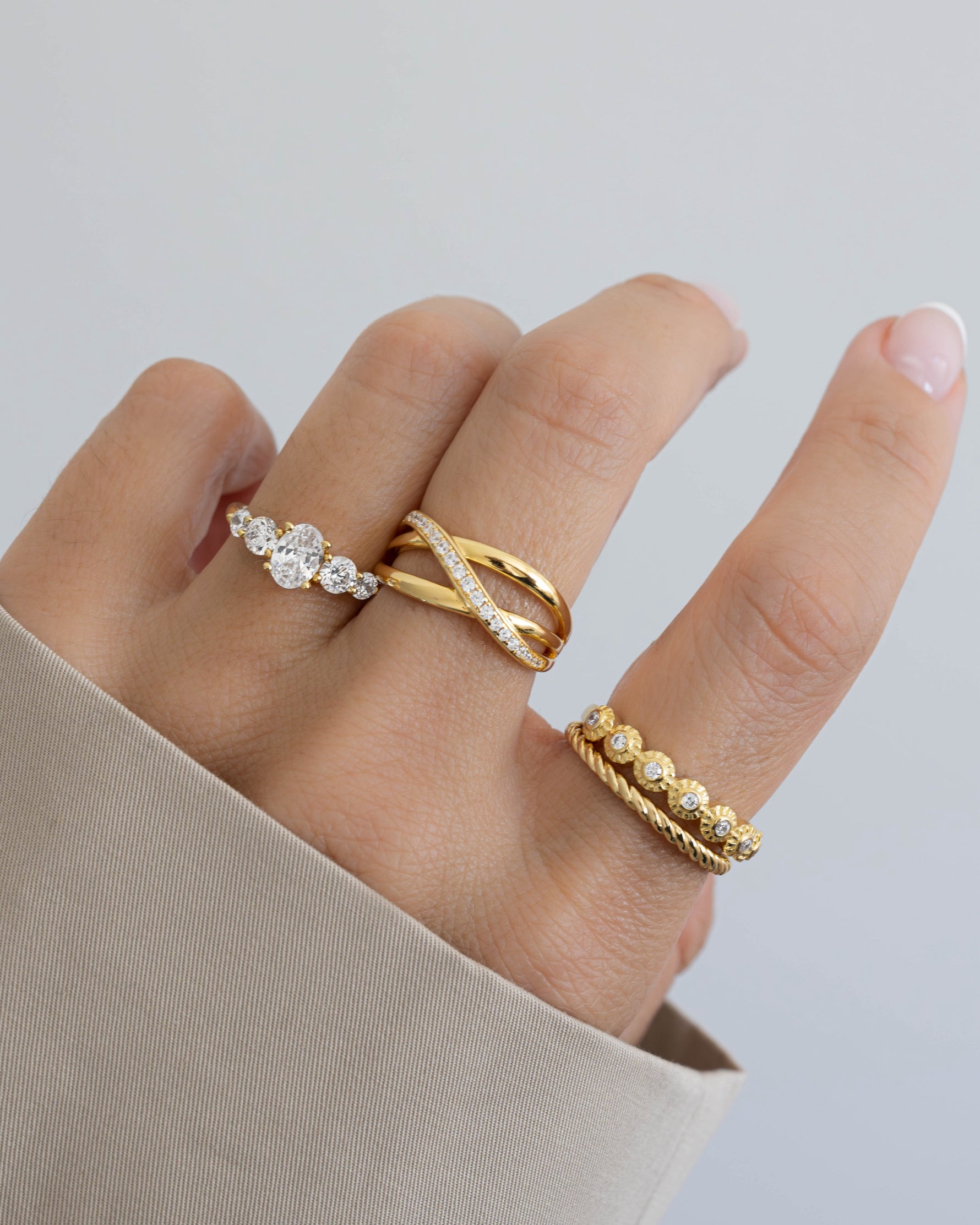 Model wearing three gold dainty rings featuring a gold oval ring, a gold statement ring, a bezel diamond ring, and a gold stackable ring.