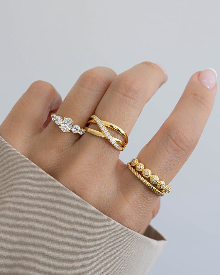 Model wearing three gold dainty rings featuring a gold oval ring, a gold statement ring, a bezel diamond ring, and a gold stackable ring.
