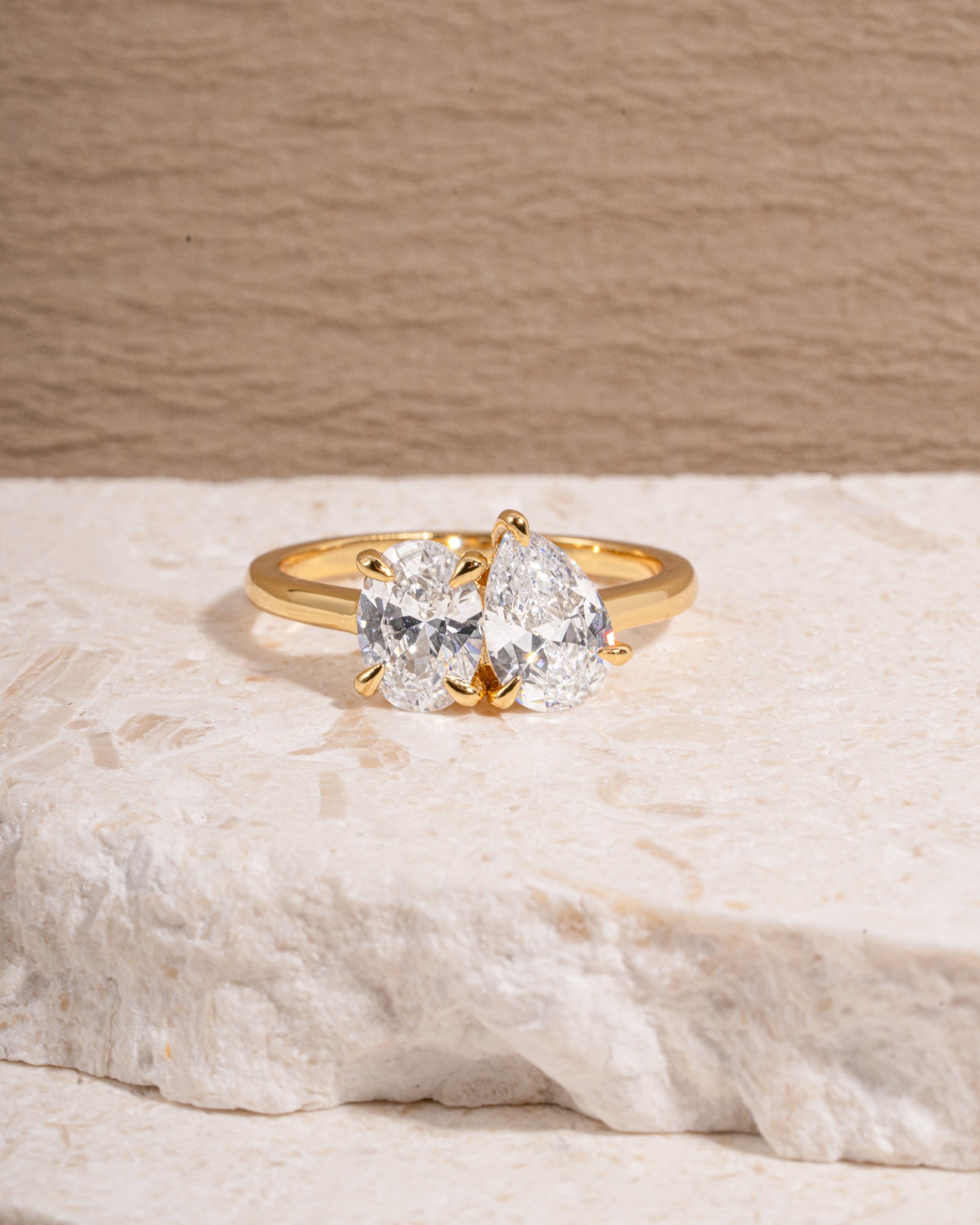 Gold diamond engagement ring with a toi et moi ring design on a textured surface