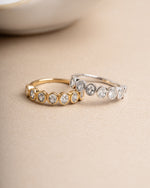 Two diamond rings, both are oval bezel set rings, one gold promise ring, and one sterling silver stacking ring, laying side by side on a neutral background 