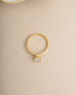 Gold diamond gemstone ring with a diamond band on a beige background