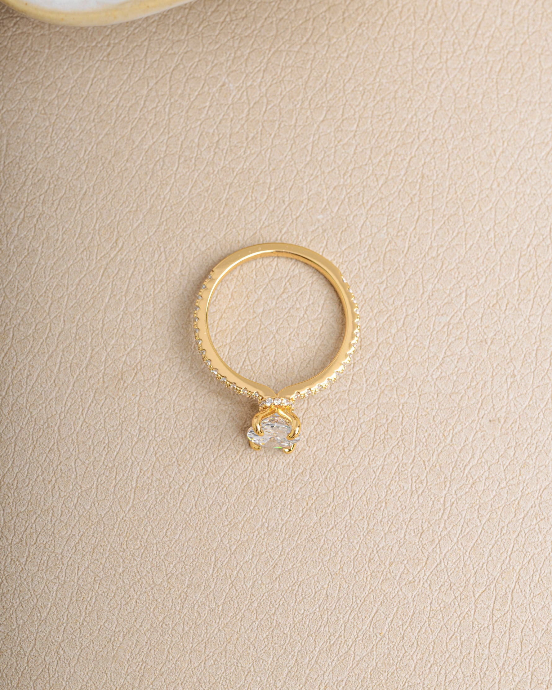 Gold diamond gemstone ring with a diamond band on a beige background