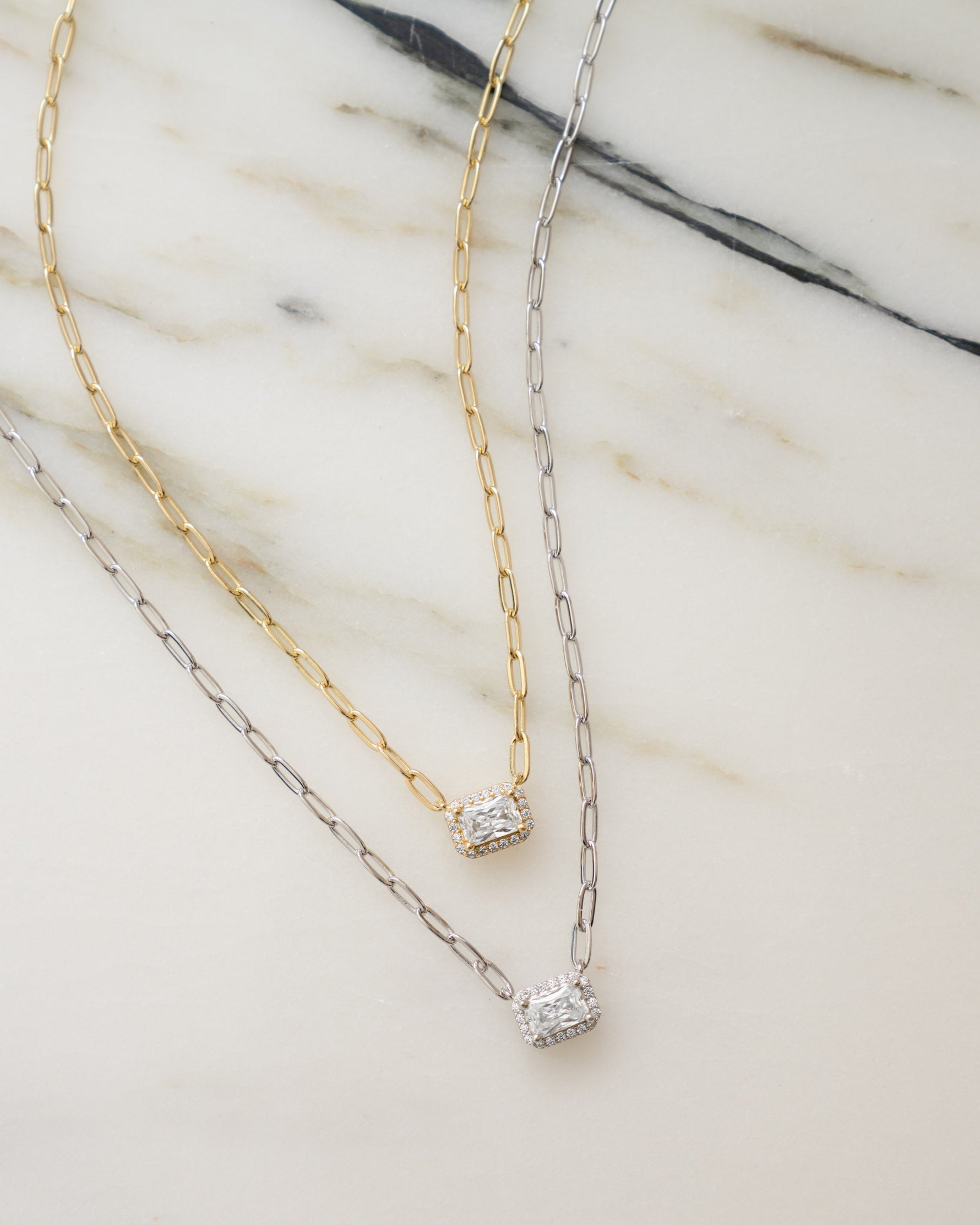 gold pendant necklace with paperclip chain laying next to a sterling silver baguette necklace