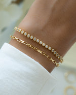 closeup image of model wearing gold bracelets featuring round bezel tennis necklace and tiny link paperclip bracelets