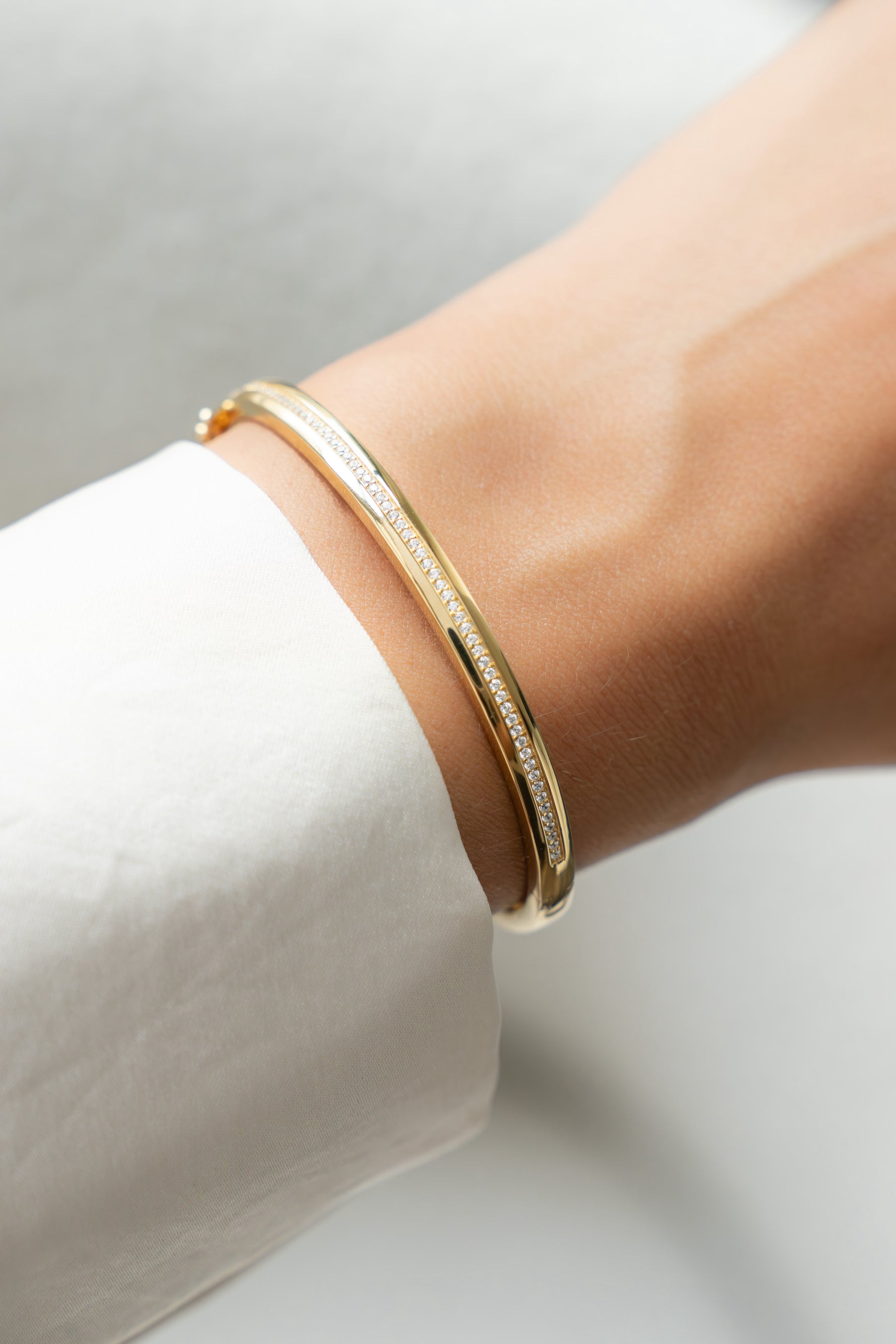 Gold diamond bangle bracelet on a wrist with a white background
