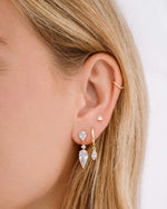 Model wearing gold pear drop dangle earrings, charm huggie earrings, and pear cut diamond stud earrings