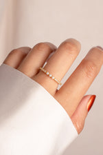 Gold three pearl ring with tiny diamond accents on a finger with a plain background
