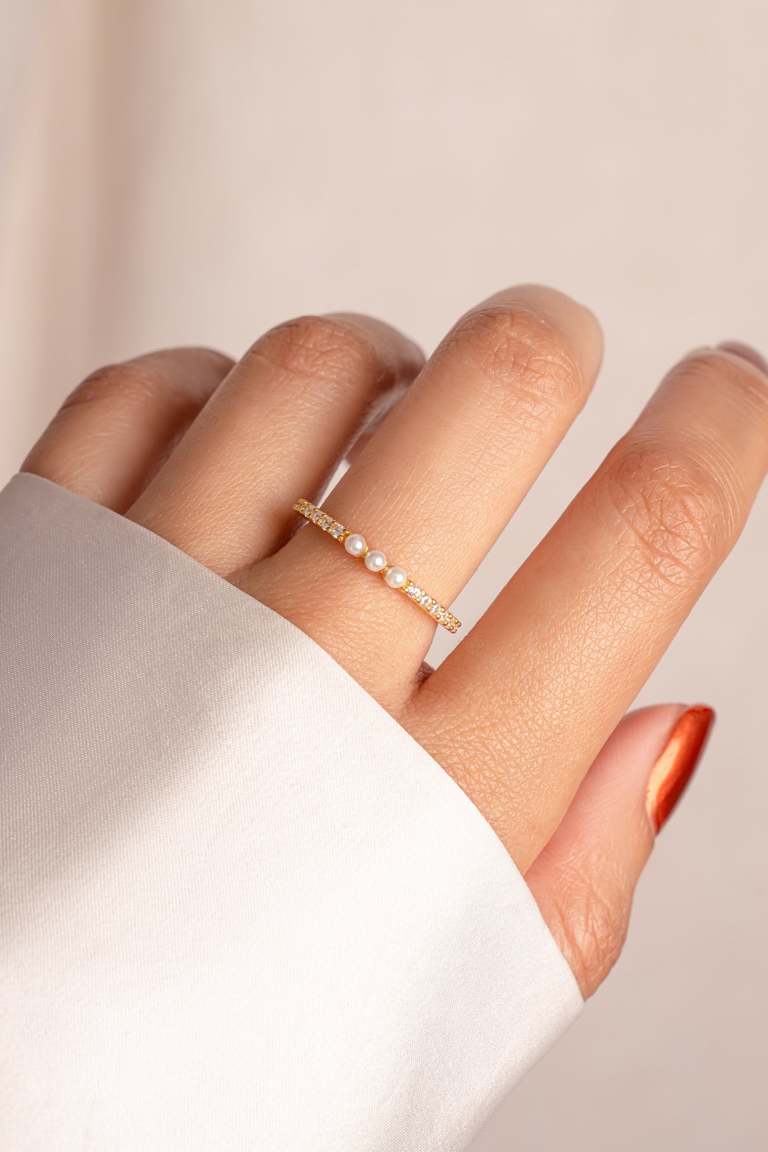 Gold three pearl ring with tiny diamond accents on a finger with a plain background