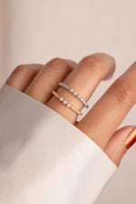 Close-up of a hand wearing pearl rings on a neutral background