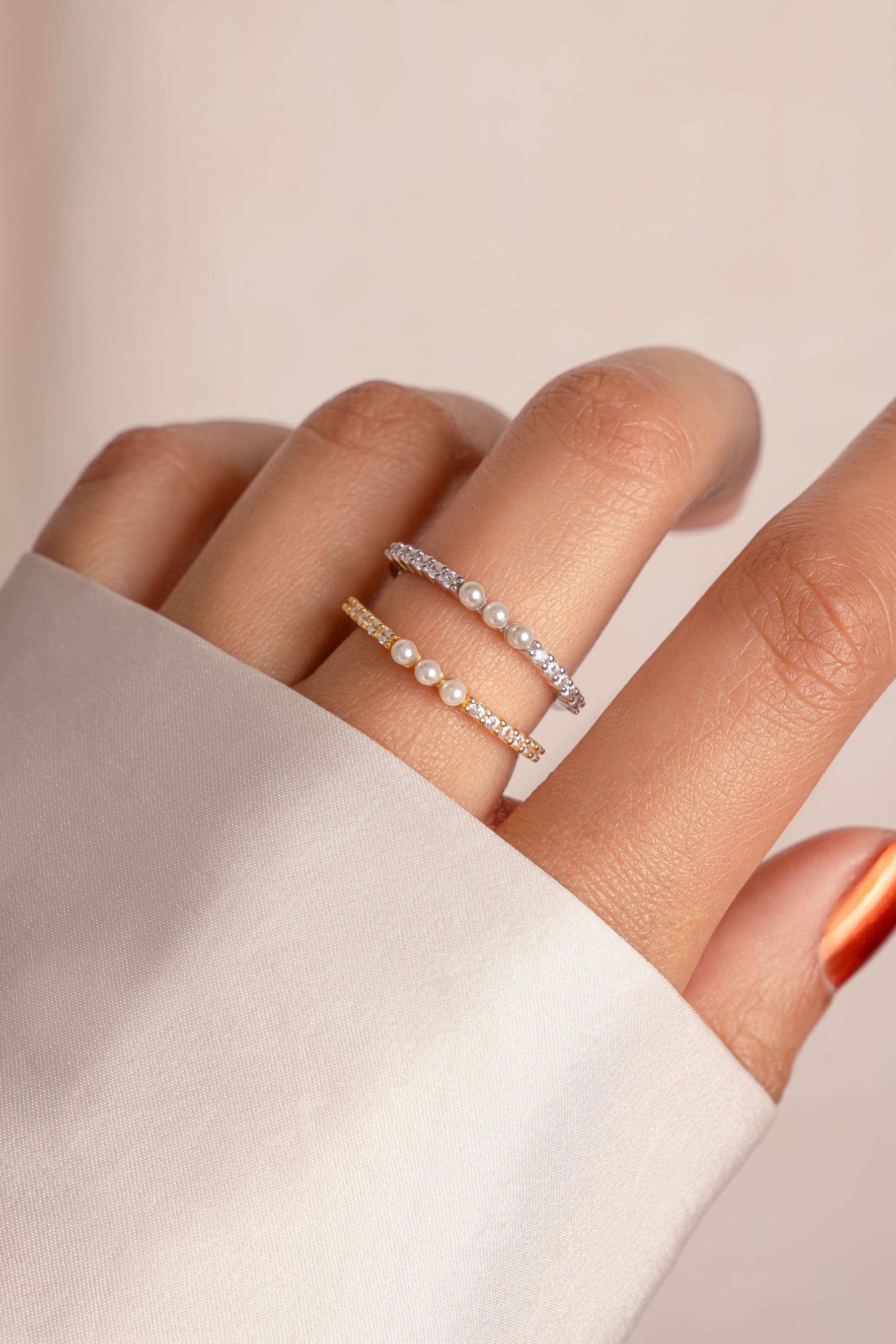 Close-up of a hand wearing pearl rings on a neutral background