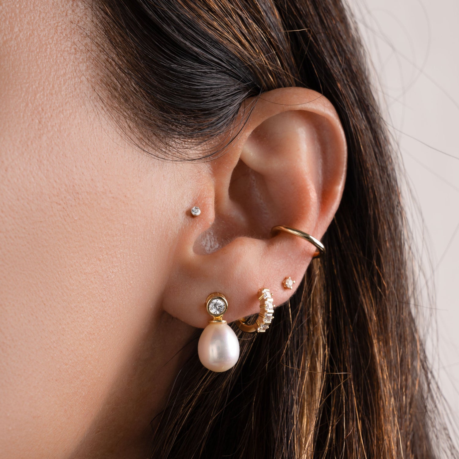 model wearing wedding earring stack featuring gold freshwater pearl and cubic zirconia dangle earrings, a mini hoop, a pearl stud earring and a simple ear cuff