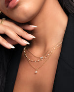 model wearing gold necklace stack featuring a freshwater pearl pendant necklace, a opal beaded necklace and a baguette necklace with a cubic zirconia stone