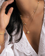 Model wearing a delicate gold necklaces with a white lace top featuring a beaded pearl necklace, a baguette diamond necklace, and a sunflower pendant necklace