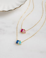 fatlay image of toi et moi birthstone necklaces with custom birthstone gemstone, one gold necklace features a ruby and rose birthstone, while the other gold necklace features a sapphire and aqua birthstone