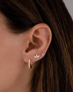 closeup image of model wearing cubic zirconia studded hoop earrings, dainty gold petal stud earrings, and a solitaire stud earrings