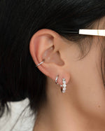 Model wearing sterling silver hoop earrings and a dainty silver ear cuff.