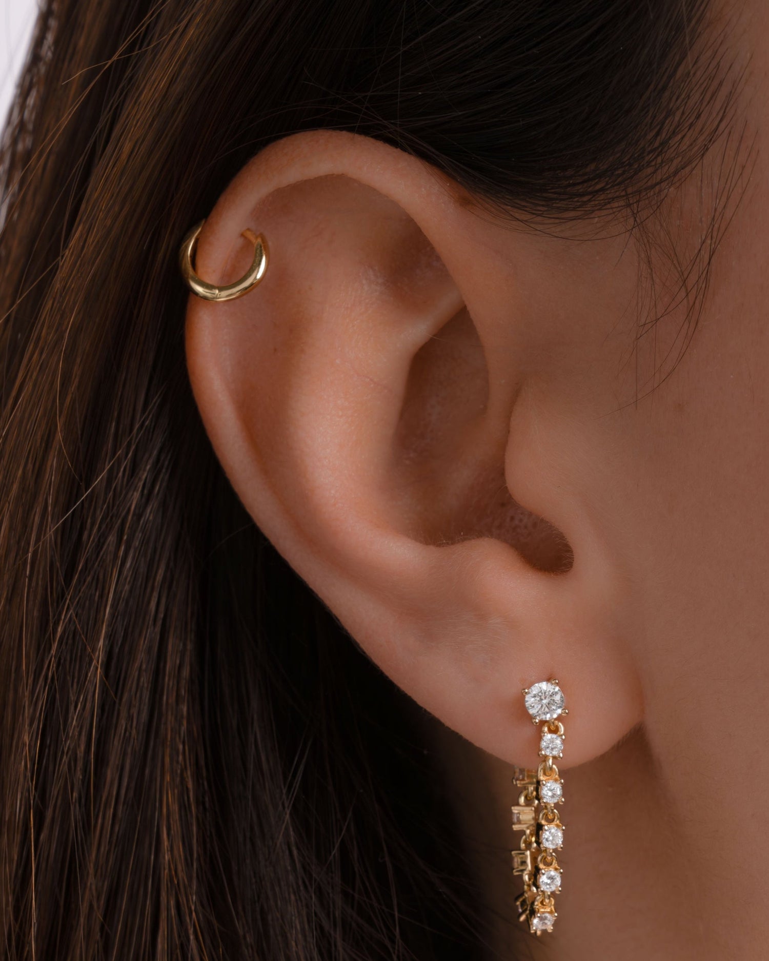 Close-up of an ear wearing gold hoop cartilage earring and a cz drop earring 