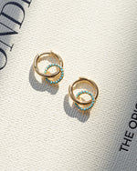 gold dangle earrings with turquoise charms laying on a fashion book